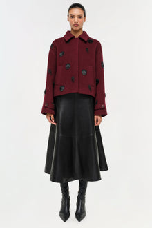 Black leather midi skirt with A-line silhouette and center seam, styled with burgundy patterned jacket.