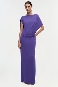 Woman wearing a purple floor-length gown with draped short sleeves and ruched waist detail.