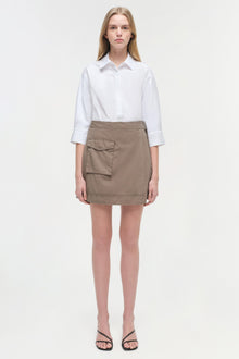 Woman wearing white collared button-up shirt with three-quarter sleeves and taupe mini skirt with front patch pocket.
