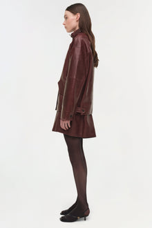 Burgundy leather jacket worn over a matching skirt, shown from the side on a model wearing dark tights and black heels.