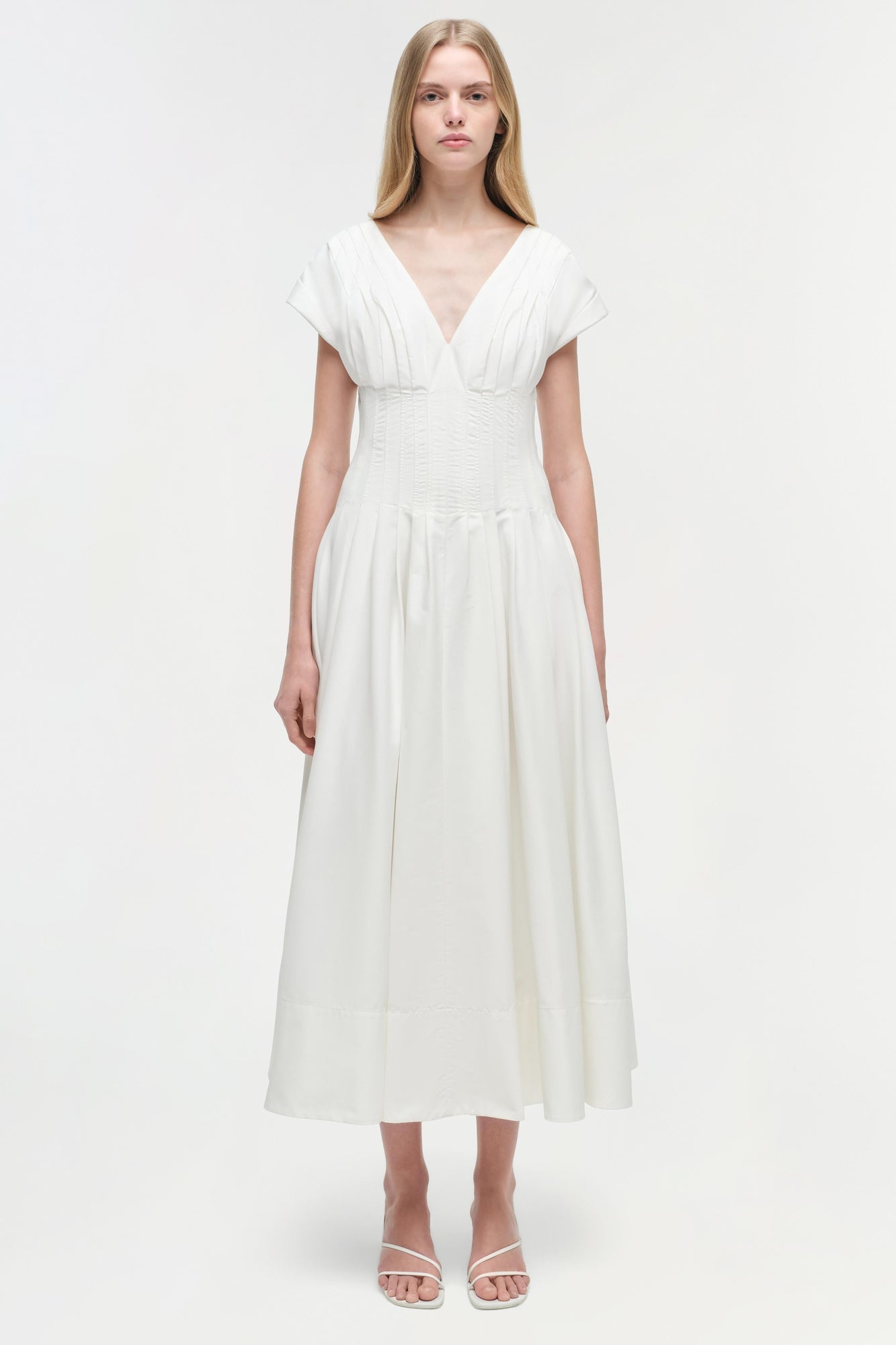 Woman wearing a white cotton midi dress with short sleeves, V-neckline, and gathered waist detail.