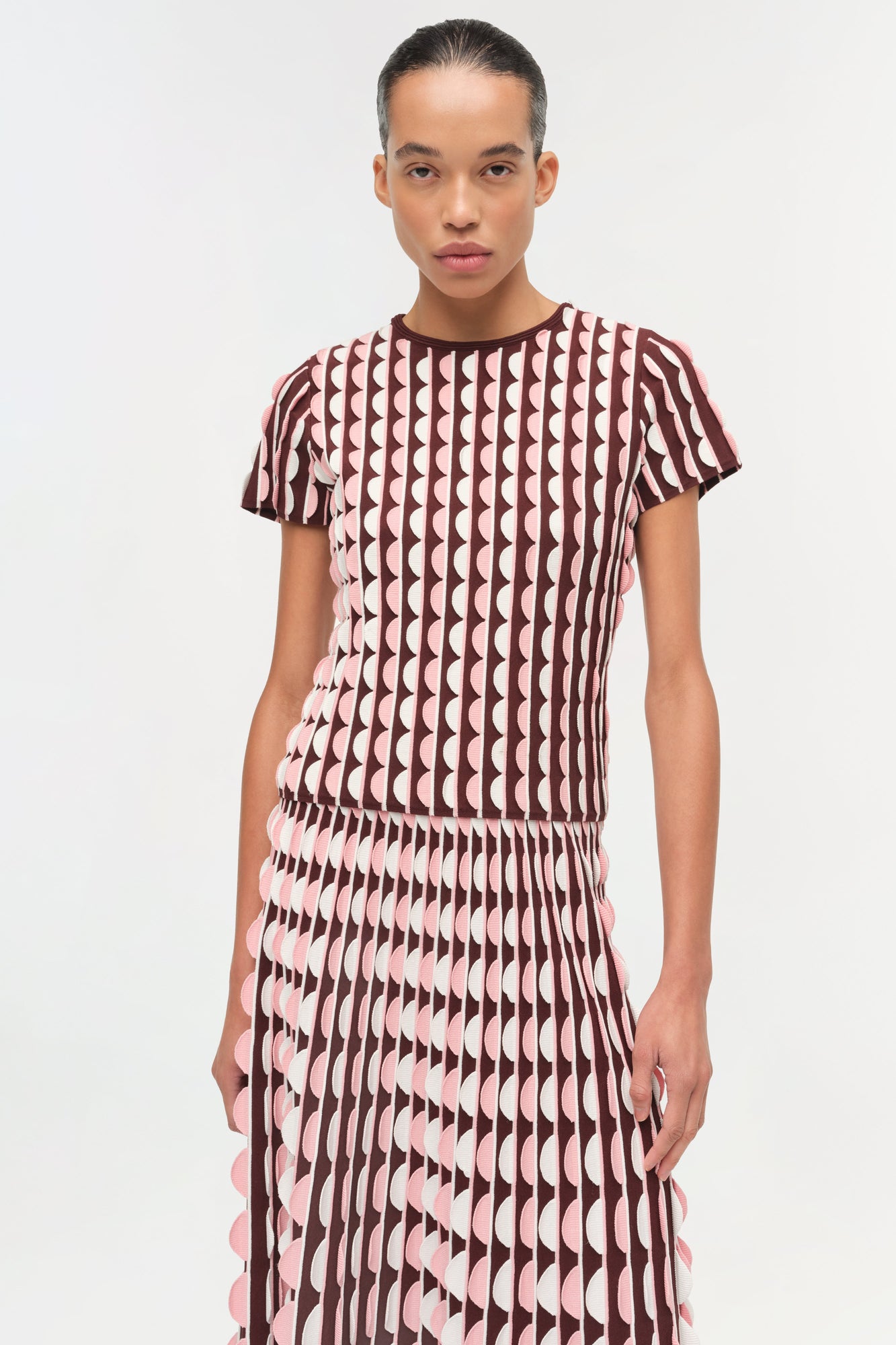 Brown and pink knit midi skirt with scalloped edges worn with matching short-sleeve geometric patterned top.