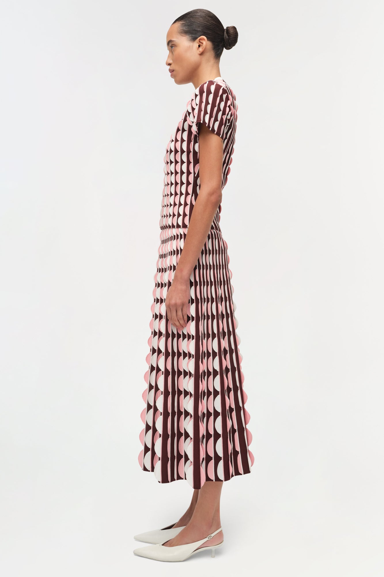 Burgundy and cream knit midi skirt with geometric pattern and scalloped hem edges, shown on model from side view.