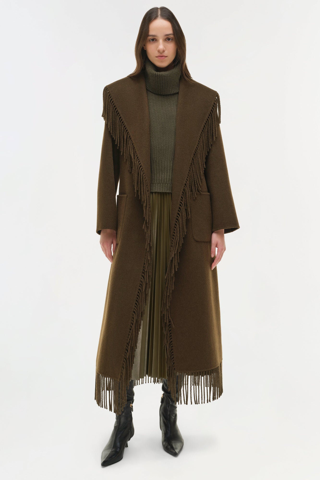 Olive wool coat with fringe trim along the front and hem, worn over a turtleneck sweater.