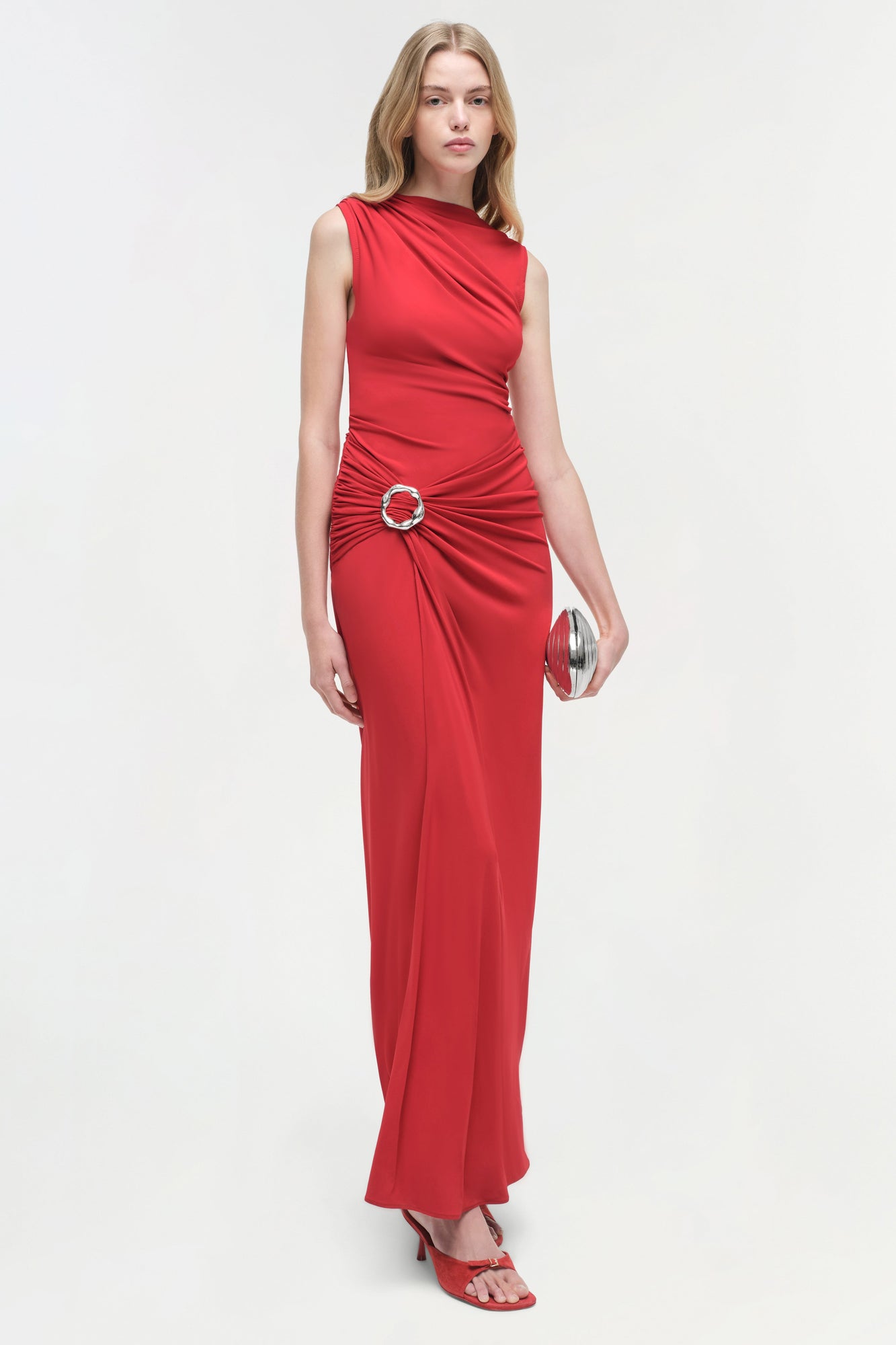 Red sleeveless jersey gown with ruched waist detail and circular ring accent.