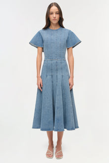 Woman wearing light blue denim dress with short sleeves, vertical seaming detail, and full midi skirt.