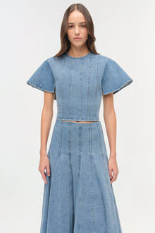 Light blue denim top with short flutter sleeves, vertical seam detailing, and a fitted waist with brown belt accent.