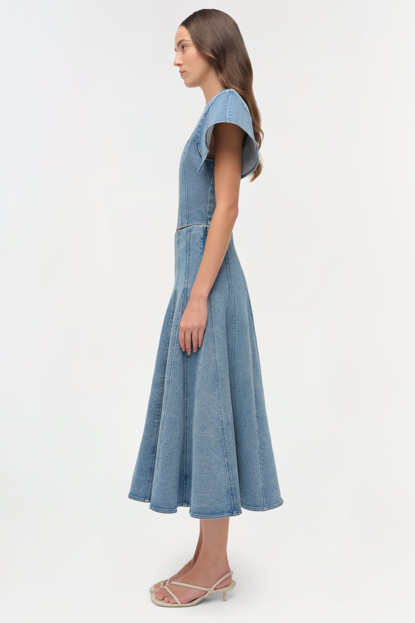 Light blue denim dress with short sleeves and fitted bodice transitioning to a full skirt, shown on model in profile view.