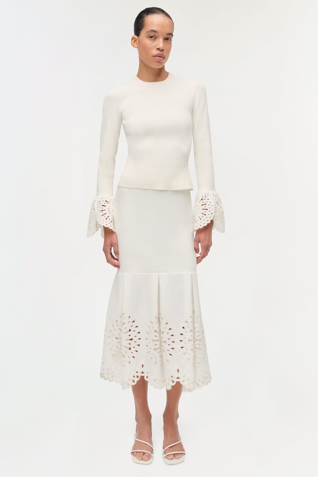Cream knit midi skirt with openwork embroidered hem and pleated waist detail, worn with matching long-sleeve top.