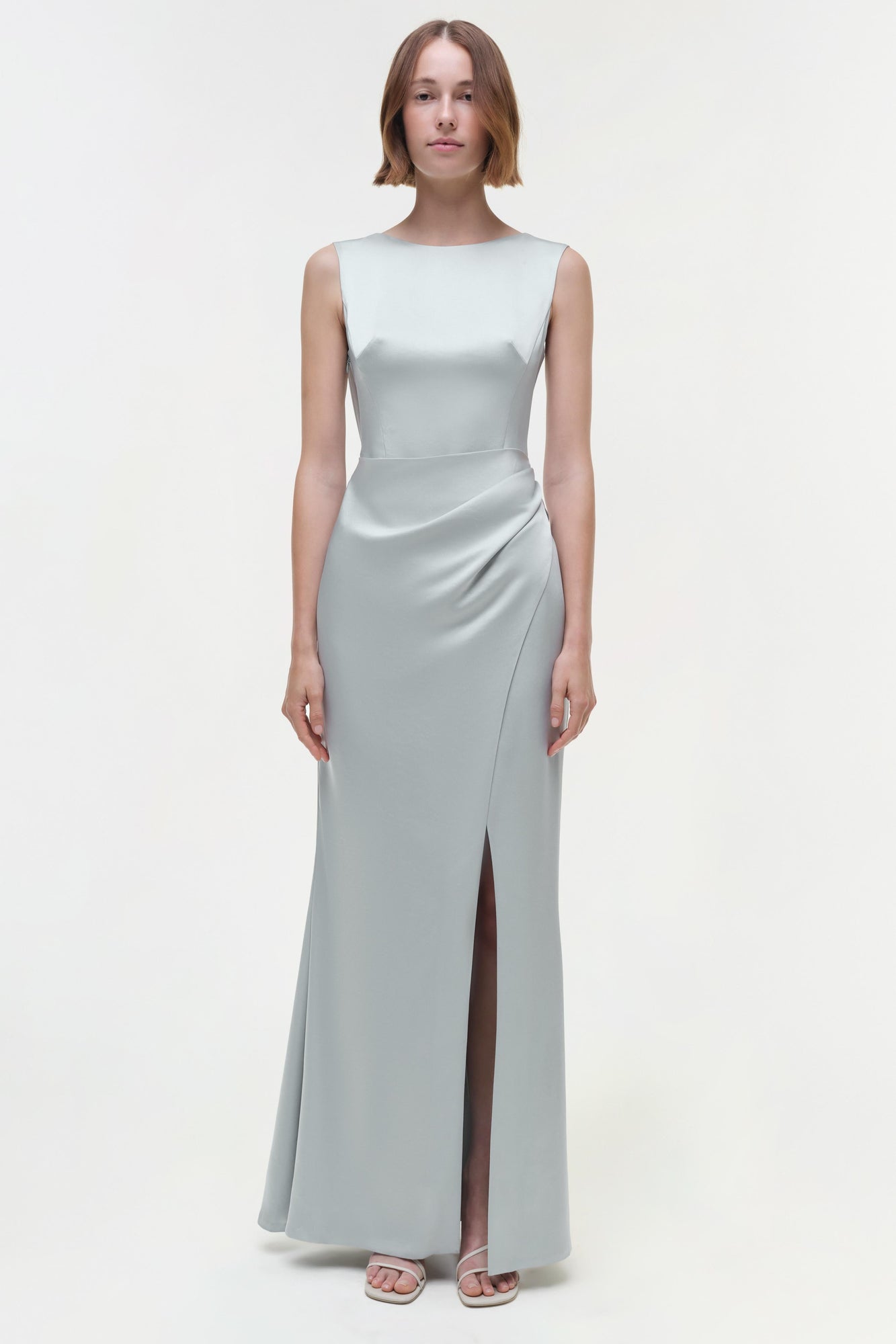 Light gray sleeveless floor-length gown with ruched waist detail and side slit, worn with flat sandals.