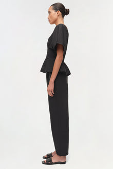 Black cotton faille top with short sleeves and peplum waist, styled with matching ankle-length pants.