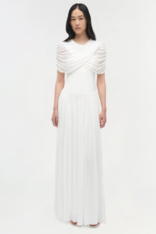 White jersey maxi dress with draped cape overlay and pleated skirt.