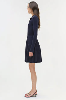 Navy ribbed knit mini dress with long sleeves and pleated skirt, modeled on woman in profile view.
