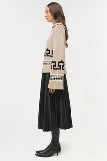 Cream V-neck sweater with black geometric patterns worn over black pleated skirt and boots.