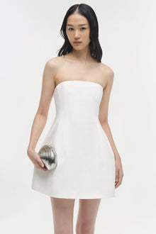 Woman wearing white strapless mini dress with fitted bodice and A-line skirt, holding silver clutch.