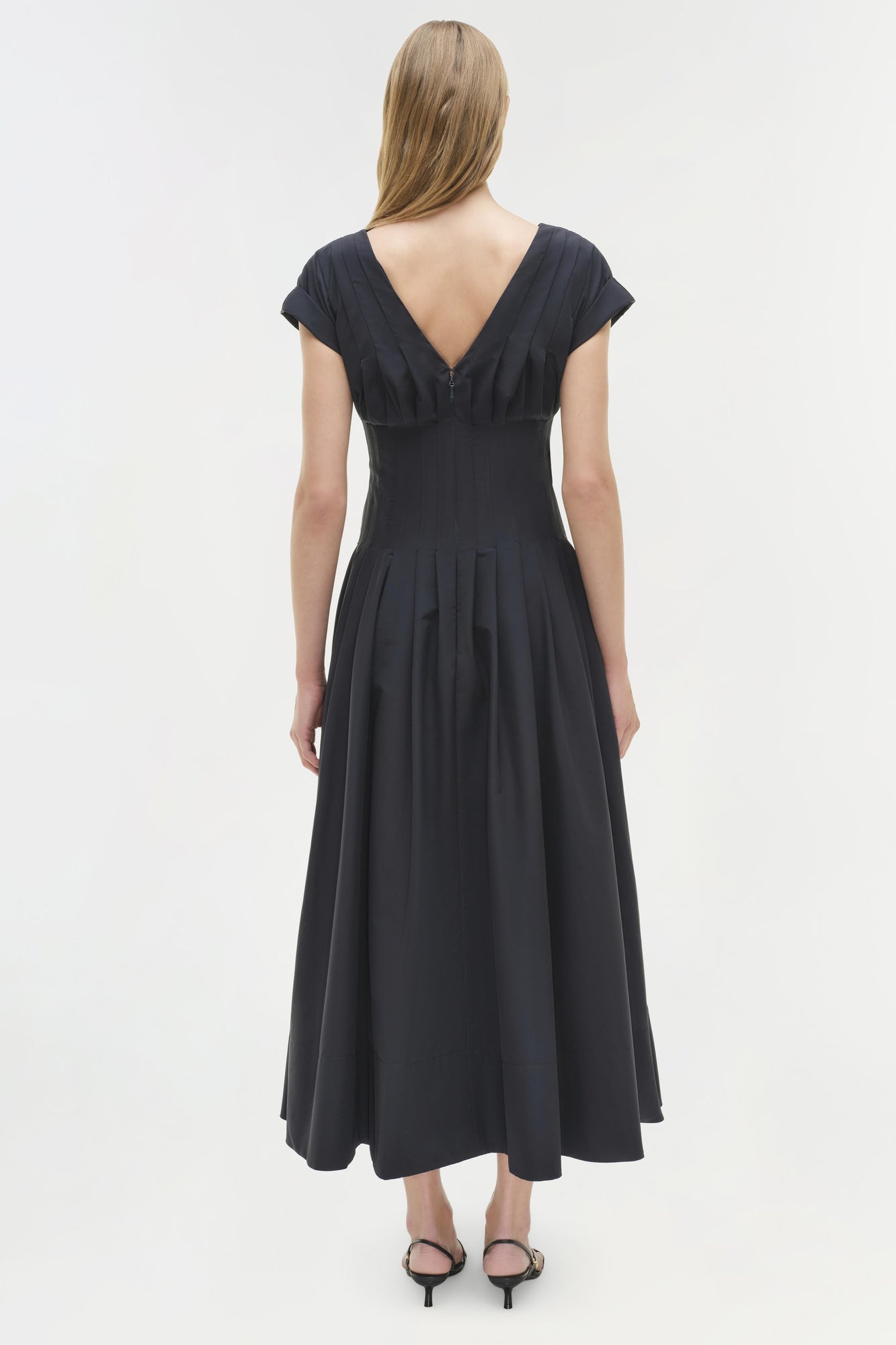 Black cotton midi dress with short sleeves, V-back neckline, and full pleated skirt, shown on model from behind.