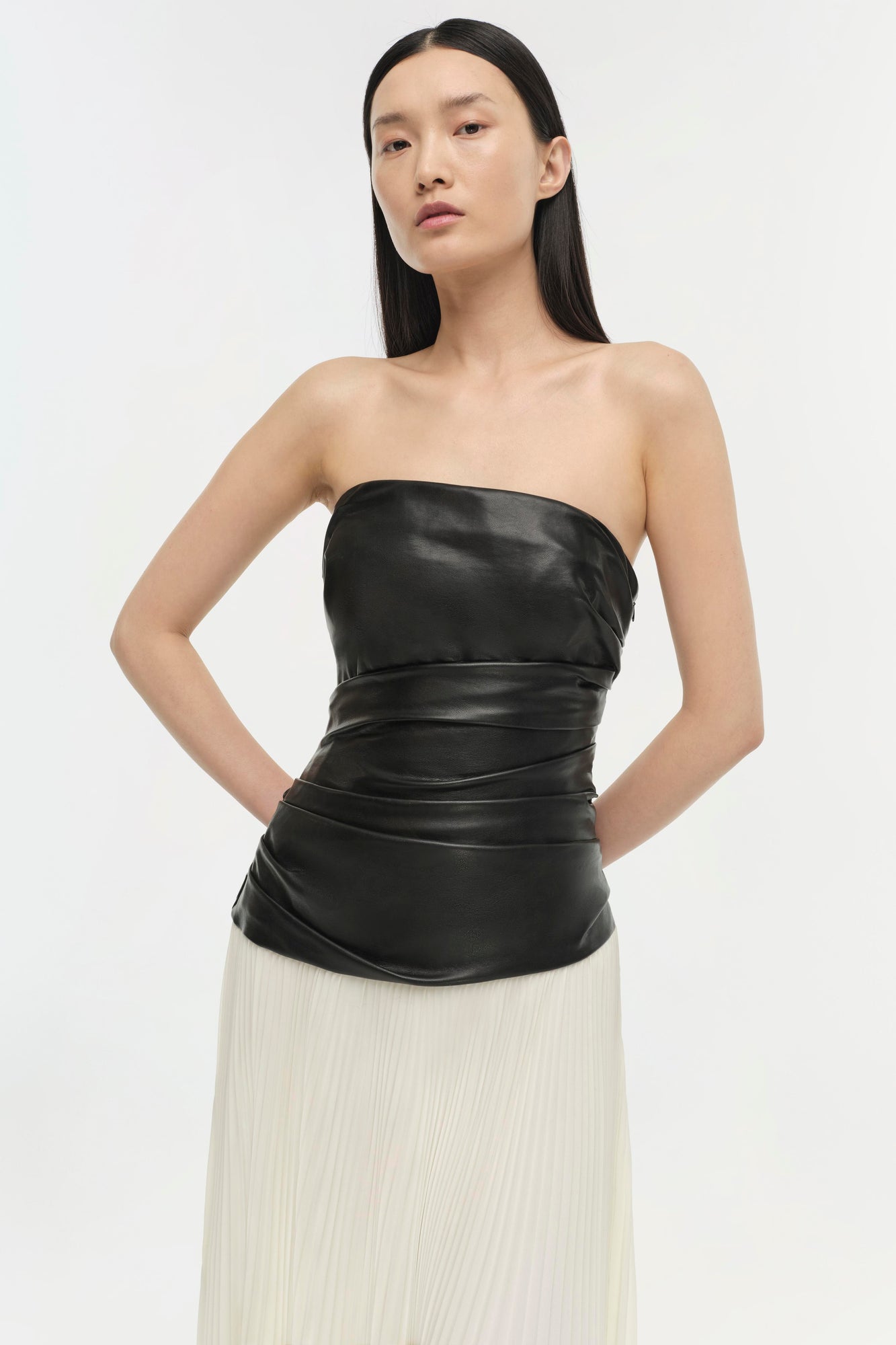 Black leather strapless top with draped waist detail over cream pleated skirt.