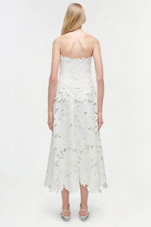 White strapless midi dress with leaf-shaped embroidered cutout details throughout, scalloped hemline, worn with clear heeled 
