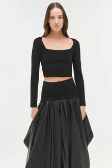 Black knit cropped top with long sleeves and square neckline, styled with matching black skirt.