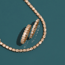 Flatlay Model A gold diamond tennis necklace and two gold diamond hoop earrings resting on a dark teal background.