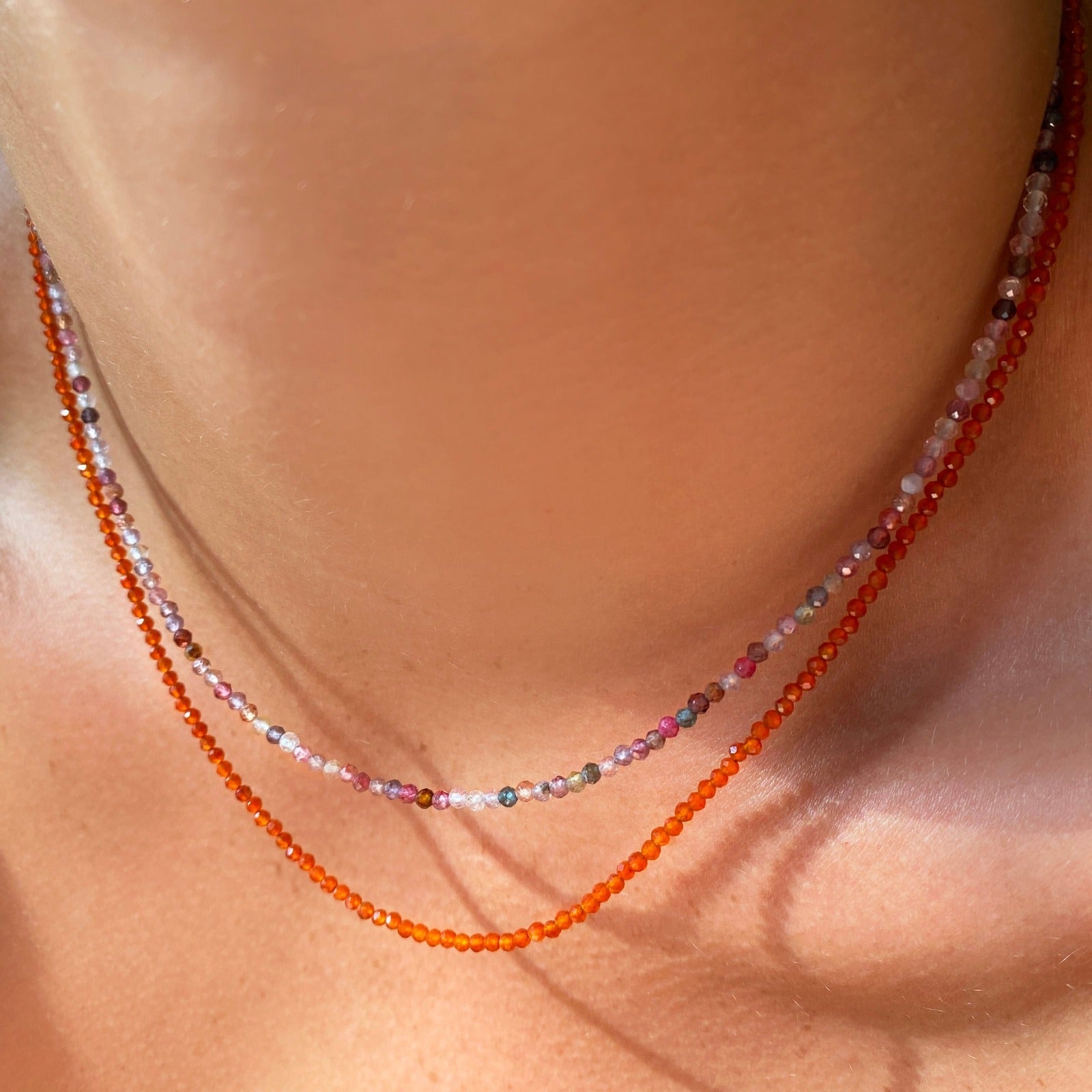 Two shimmering slim gemstone beaded necklace made of 2mm faceted stones layered together in carnelian and tourmaline on a gold linking lobster clasp on a neck
