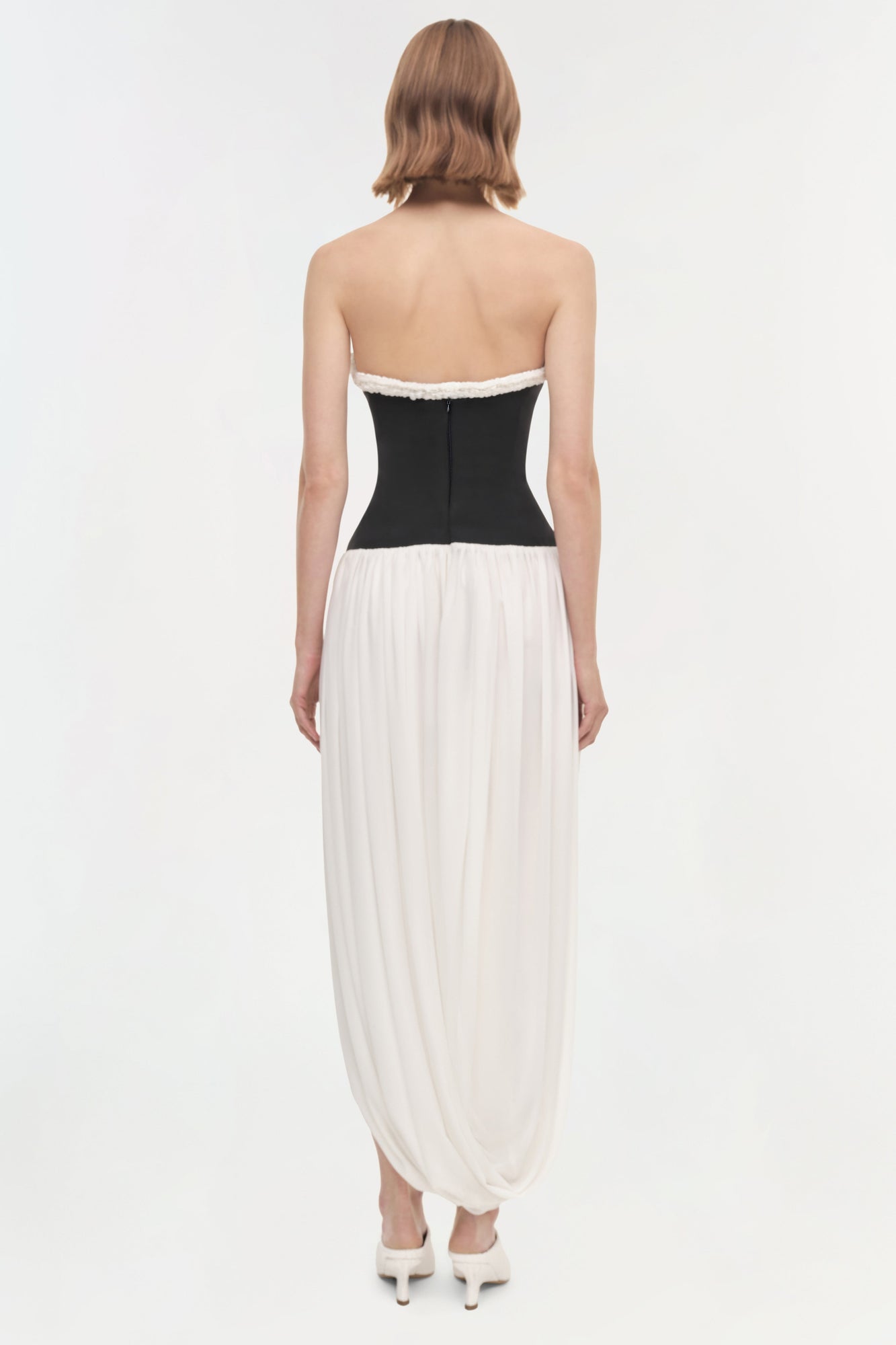 Strapless dress with black fitted bodice and white pleated draped skirt, shown from back view.
