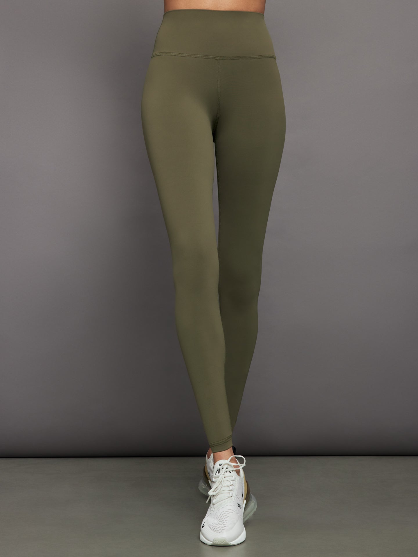 Model wears full-length olive leggings with a high-rise wide waistband and smooth, compressive fabric.