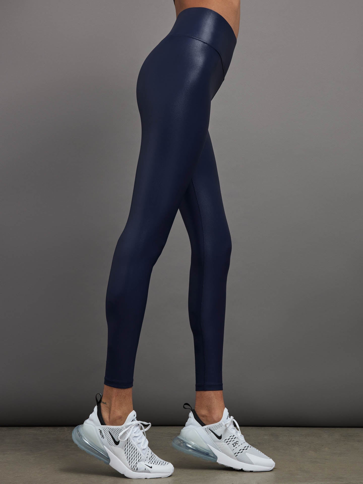 Model is wearing navy high waisted performance leggings in a liquidy-shine finish that hit at the ankle.