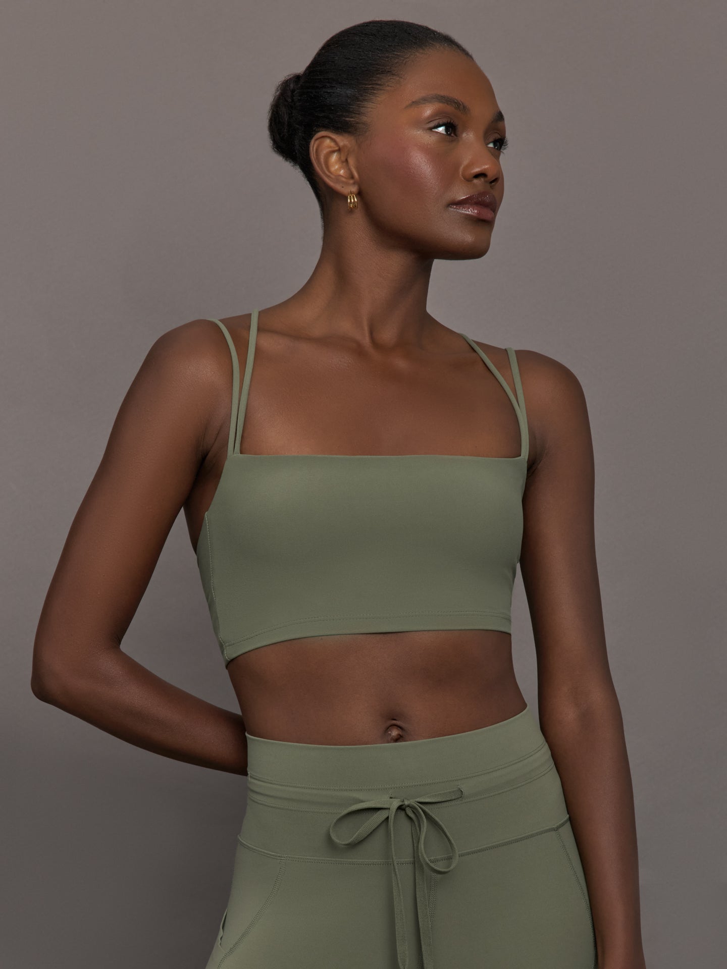 Model wears a buttery soft sports bra in army green with double straps and cross back design. 
