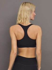 Model wears a black, ribbed, racerback sports bra with a smooth, sculpting fit.
