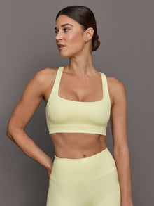 Model wears a buttery soft, ribbed pastel yellow square neck bra with a racerback silhouette. 