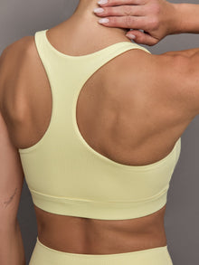Model wears a buttery soft, ribbed pastel yellow square neck bra with a racerback silhouette. 