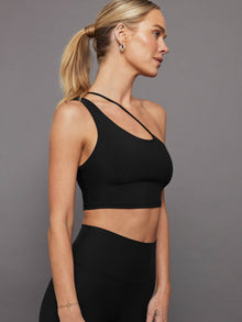 Model wears a black, sleek, one-shoulder sports bra with a smooth, body-hugging fit and an adjustable strap.
