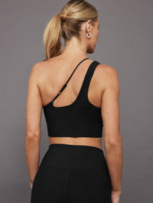 Model wears a black, sleek, one-shoulder sports bra with a smooth, body-hugging fit and an adjustable strap.
