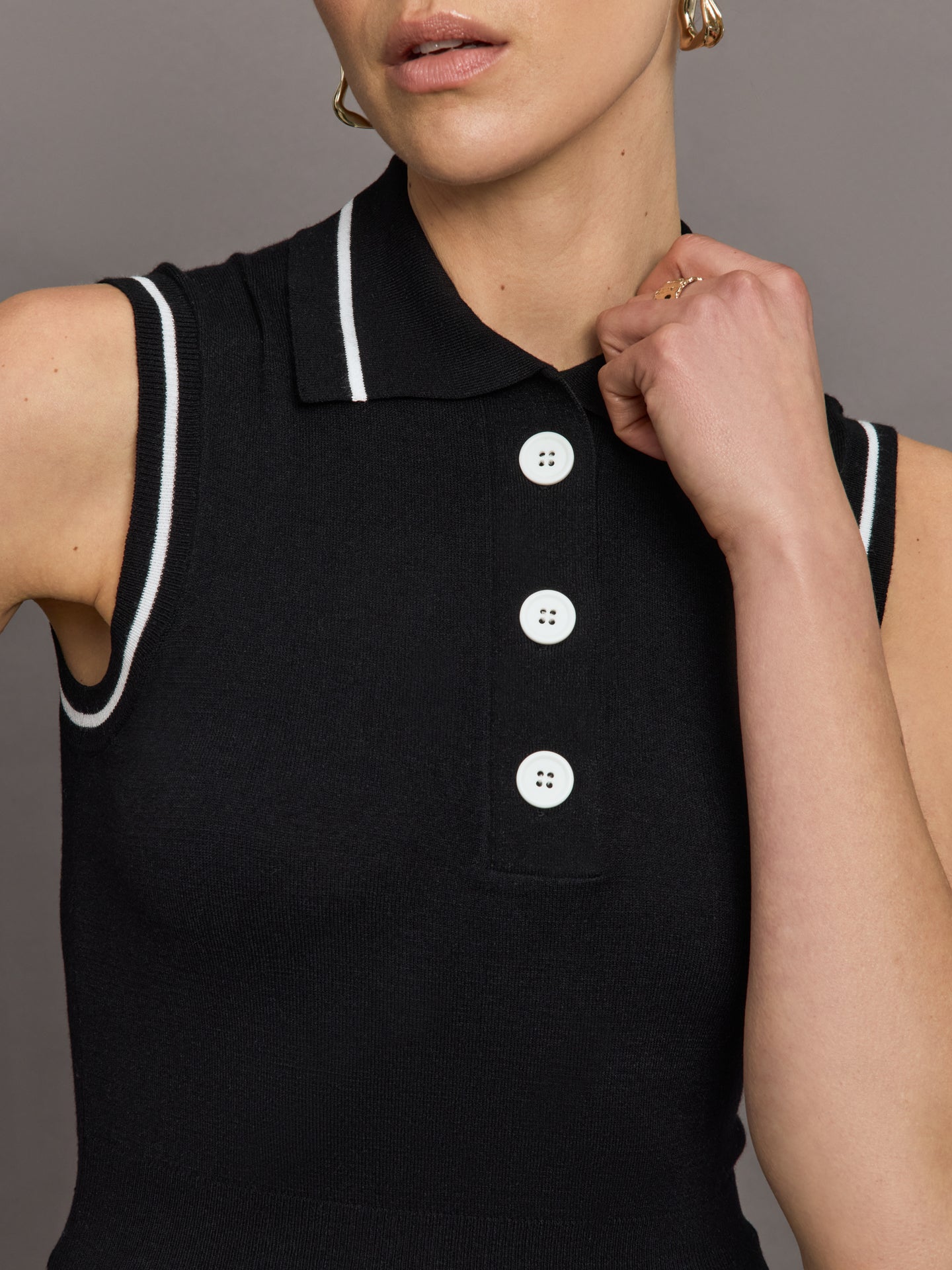 Model wears a sleeveless black tennis polo with three white buttons. 