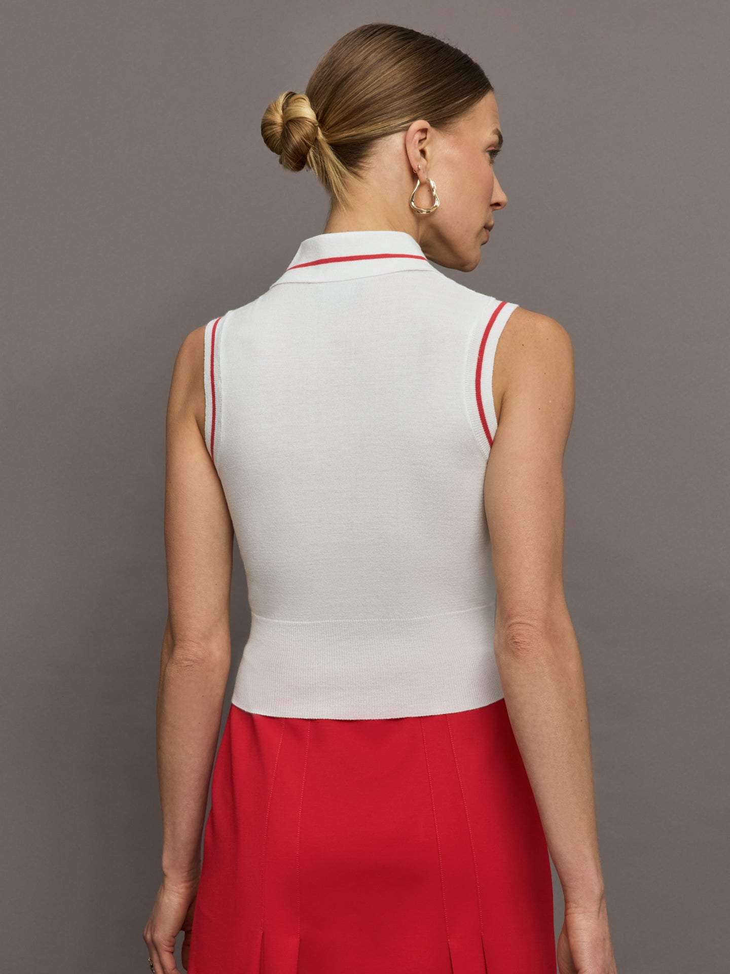 Model wears a sleeveless white tennis polo with three buttons and red seam detailing. 