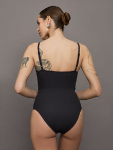 Model wears a black bodysuit with a straight neckline across the chest and thin straps. 