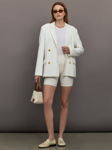 Model wears the white double-breasted blazer in Scuba, with a tailored fit, and a smooth, contoured finish.
