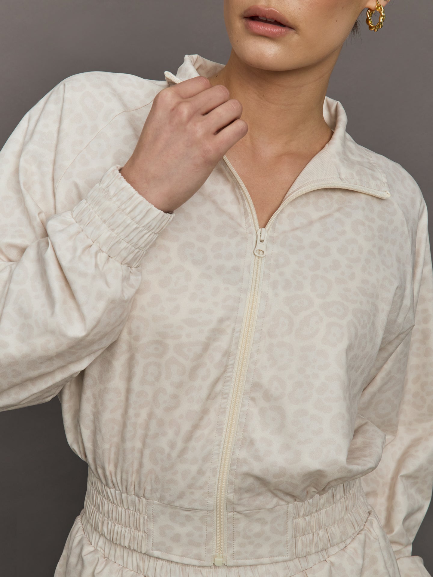 Model wears lightweight windbreaker with a snow leopard print, front zipper, and collared neck.
