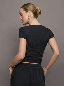 Model wears a short sleeved, ribbed jersey fitted black top with ruching down both sides. 