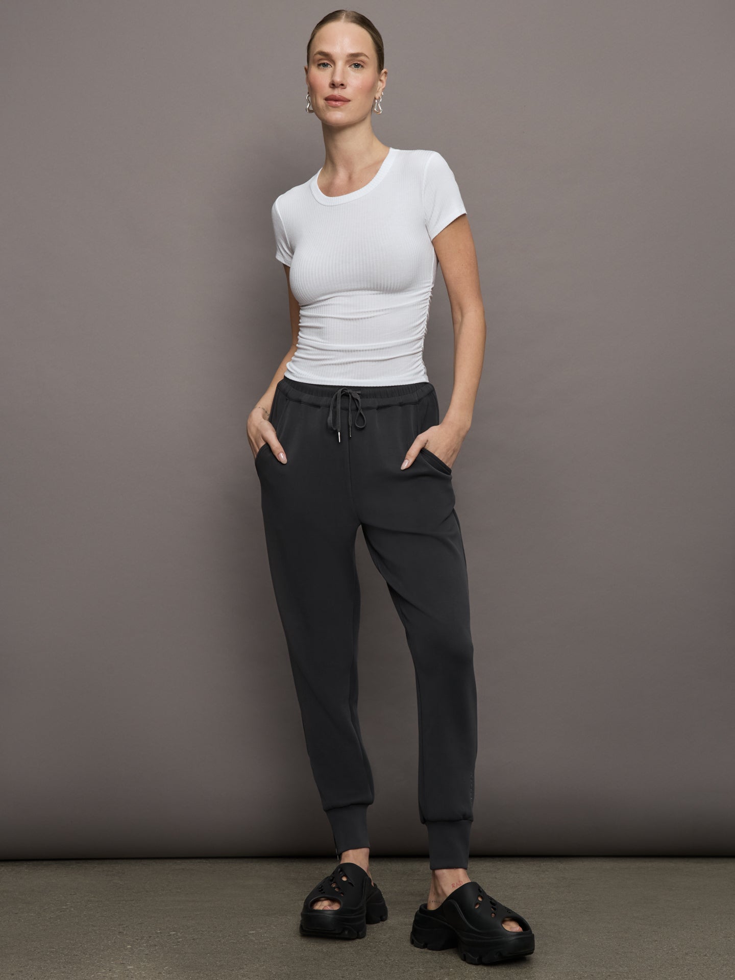 Model wears a short sleeved, ribbed jersey fitted white top with ruching down both sides. 