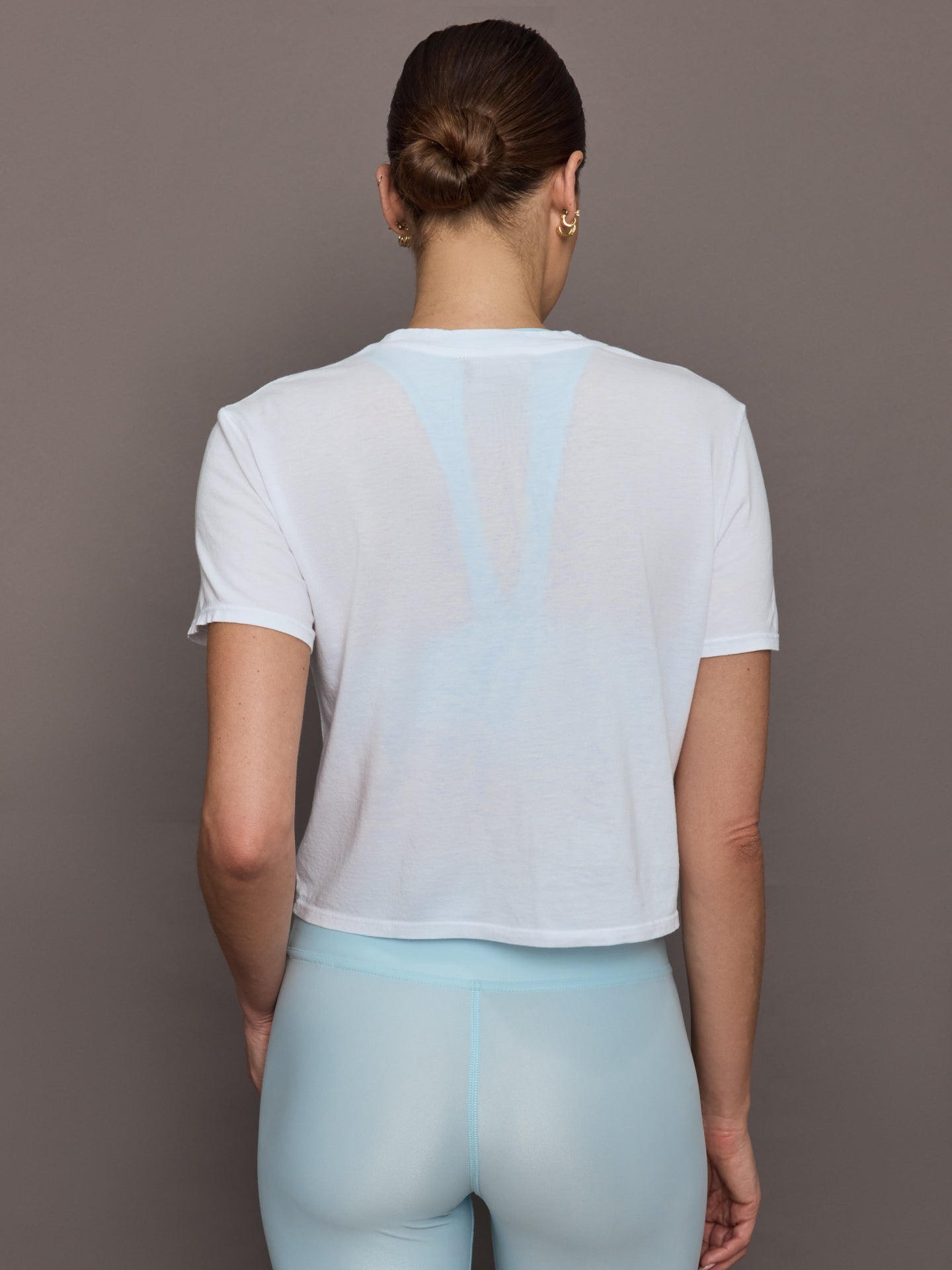 Model wears a cropped boxy white sheer tee shirt. 