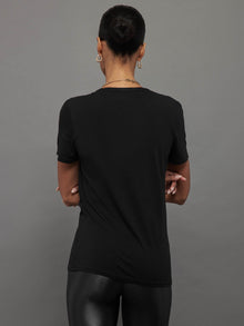 Model wears a black, short sleeve crewneck t-shirt with a front pocket and a relaxed, hip-length fit.
