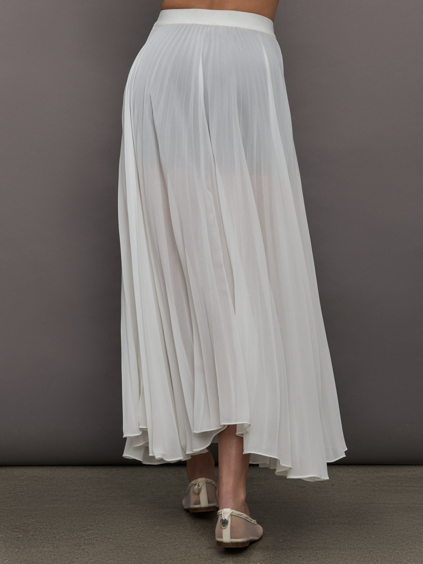 Back view of model in Mesh Pleated Skirt Ivory with flowy silhouette.