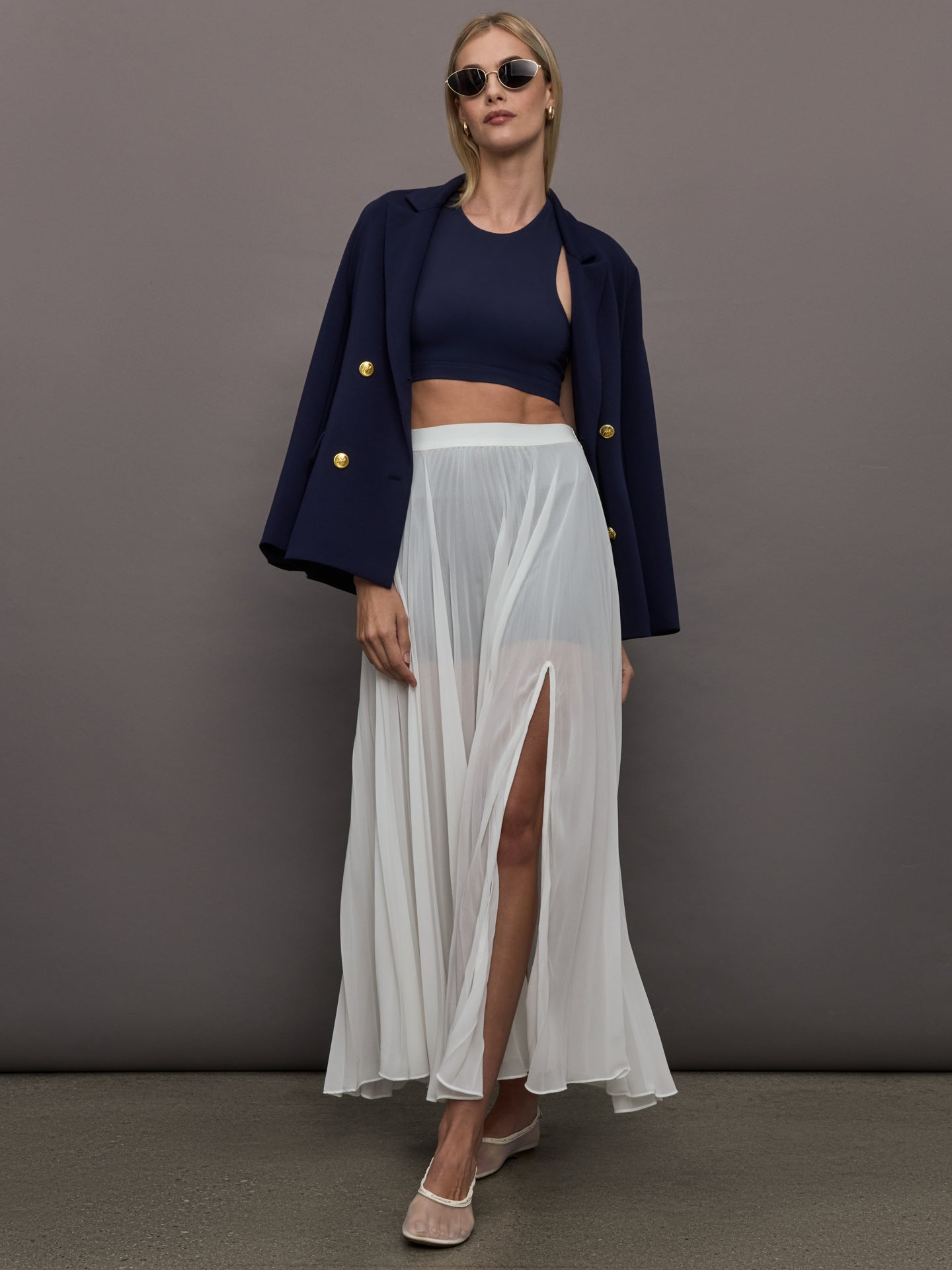 Full body view of model styled in Mesh Pleated Skirt Ivory with navy crop top and blazer.