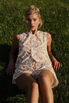 Sleeveless cream vest with orange cherry print and scalloped edges worn over matching shorts.