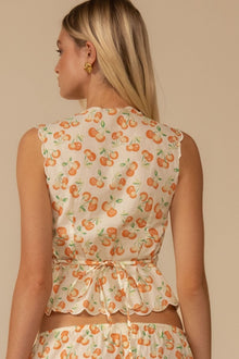 Cream sleeveless vest with orange cherry print and scalloped hem, tied at waist.