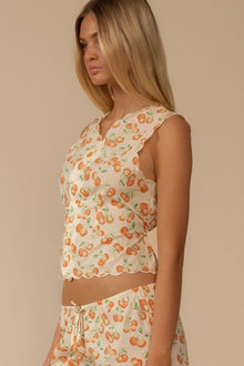 Sleeveless cream vest with orange cherry and green leaf print and scalloped trim edges.