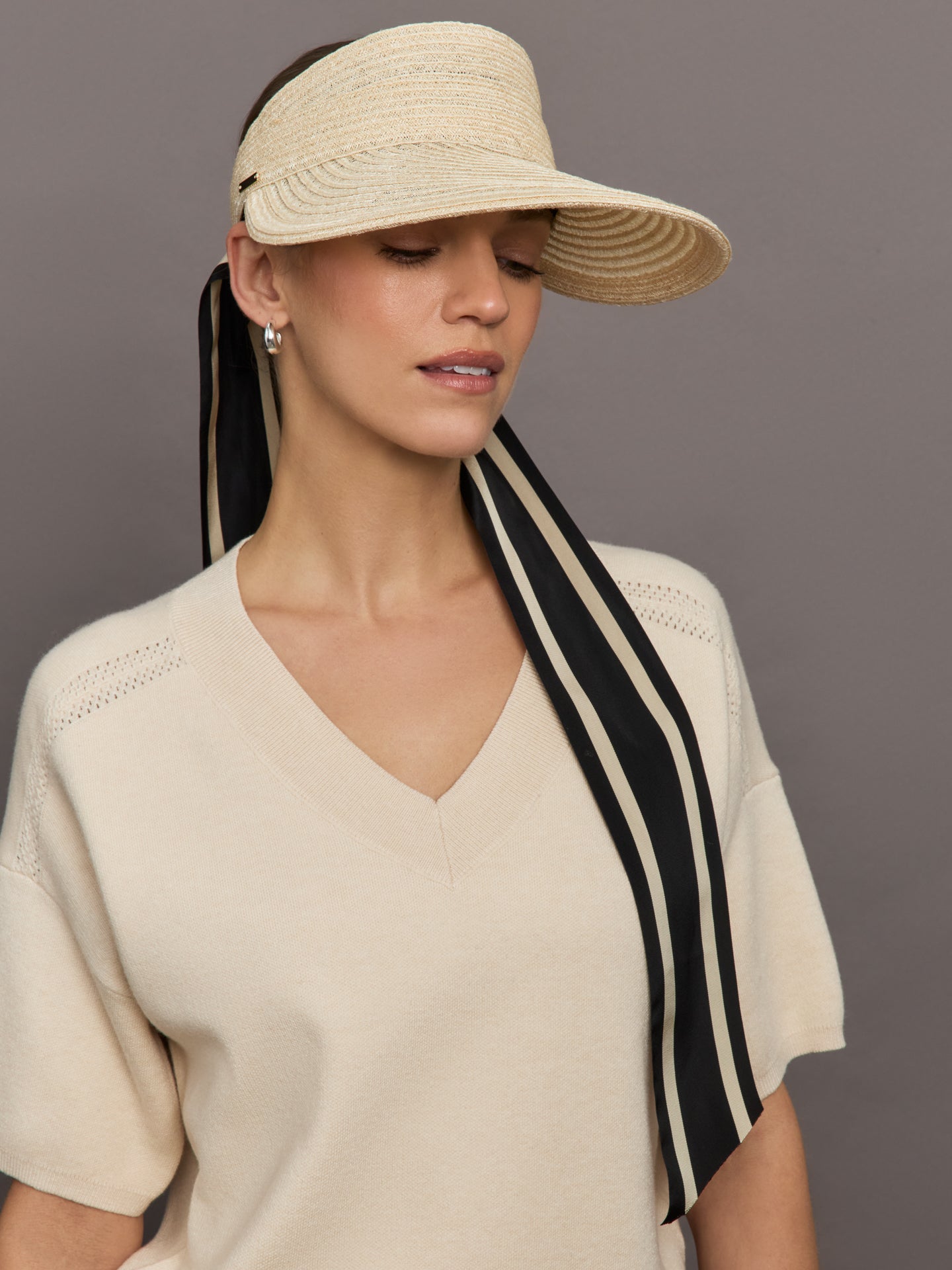 Model wears a straw visor with black and ivory ties. 