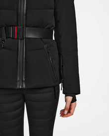 A person models the Rudsak ALAIA - 8124816 Black womens quilted ski jacket with a zipper and black belt, paired with matching black pants, shown from the waist down against a white background.